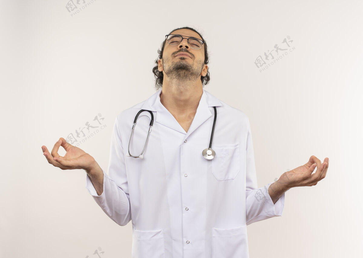 男性闭着眼睛 戴着眼镜的年轻男医生 穿着白色长袍 带听诊器 在有复印空间的隔离白墙上显示okey手势好的年轻听诊器