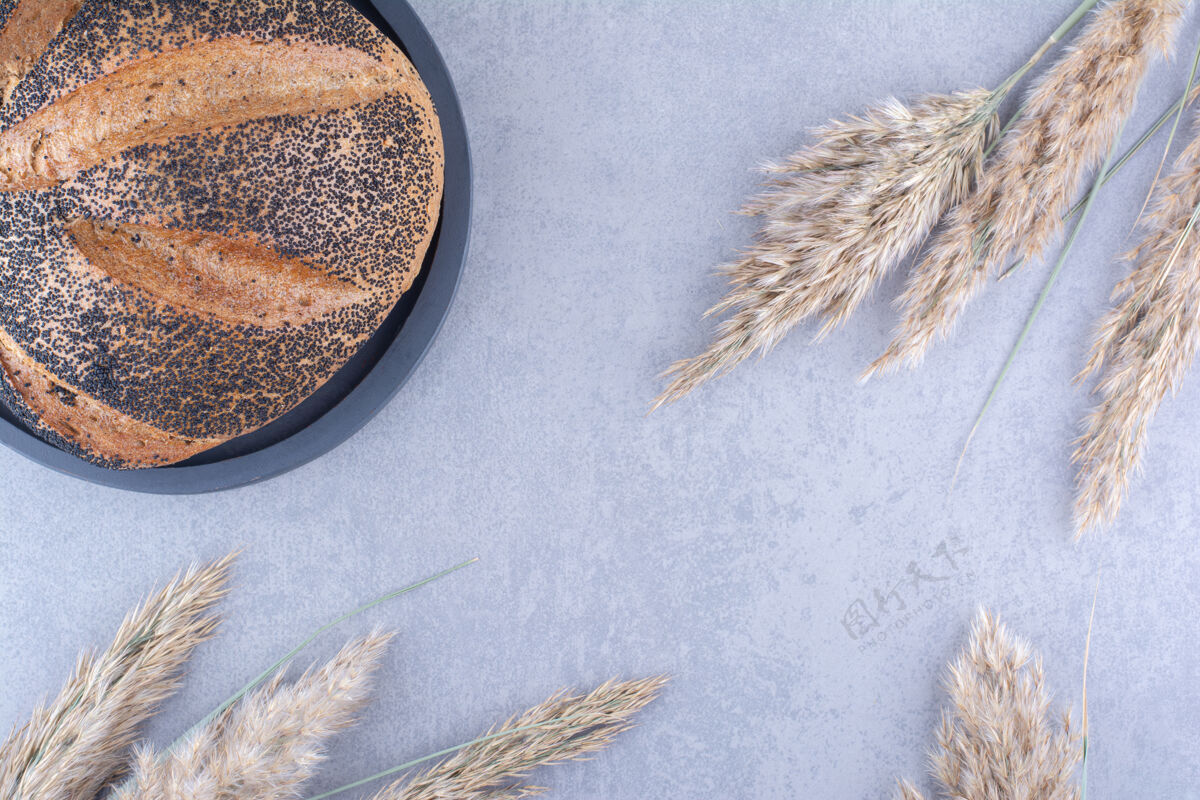 面包把涂了芝麻的面包放在盘子里 放在大理石表面的干羽毛草茎旁边羽毛草干盘子