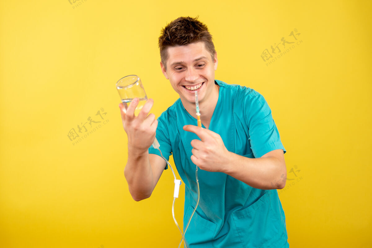 持有正面图身穿医疗服的年轻男医生拿着黄色背景上的滴管病毒听诊器滴管