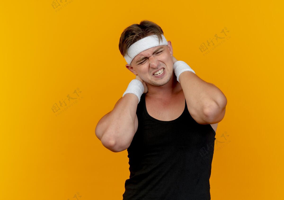 脖子疼痛的年轻英俊的运动男子戴着头带和腕带把手放在脖子后面孤立的橙色与复制空间英俊疼痛头带