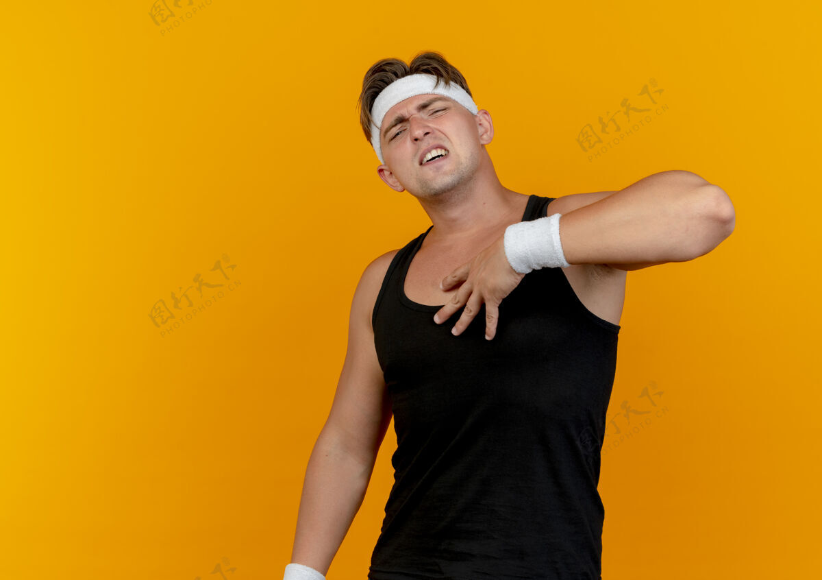 胸部疼痛的年轻英俊的运动男子戴着头带和腕带把手放在胸前隔离在橙色的复制空间帅气男人空间