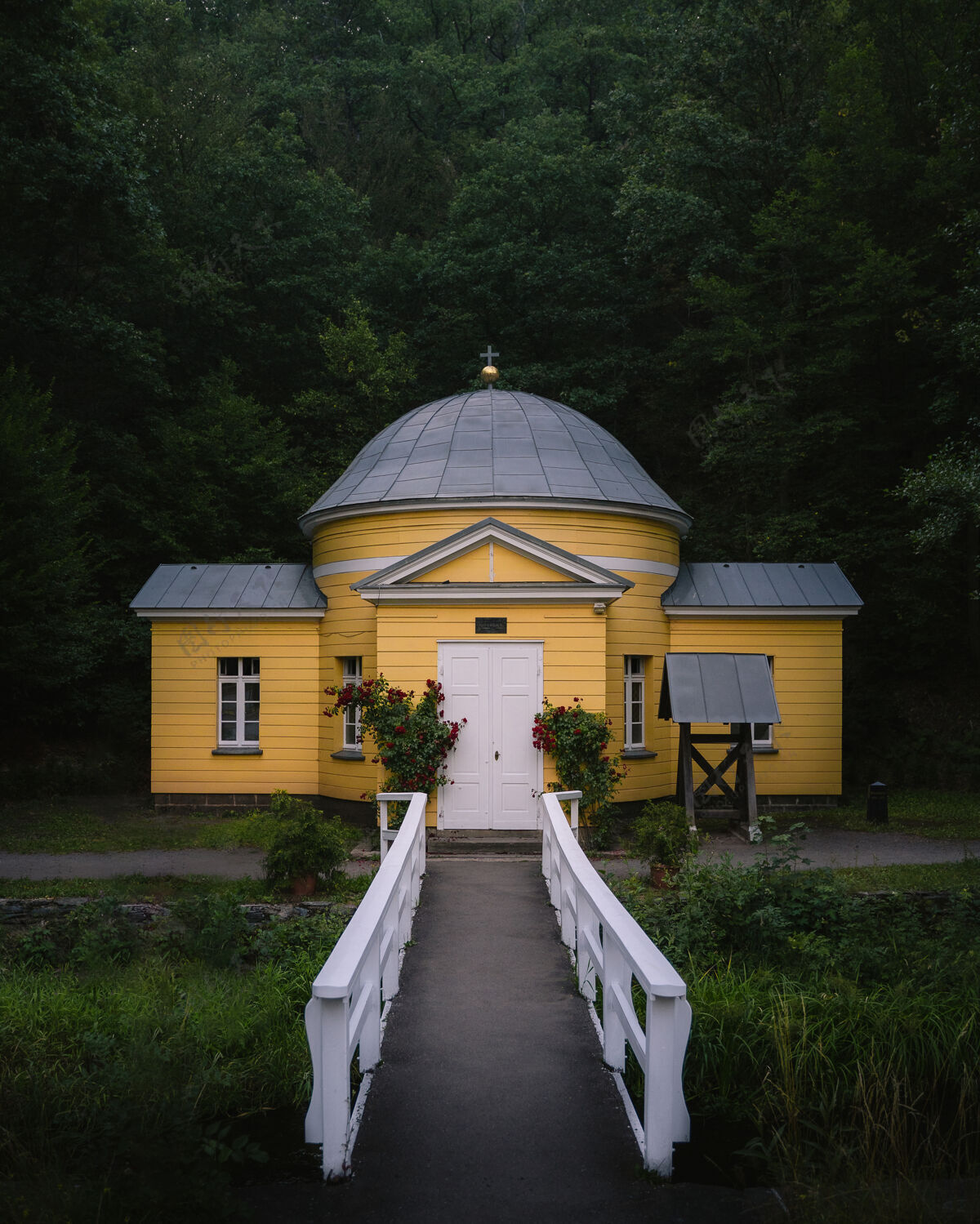 石头一个黄色基督教设施的垂直正面照片 在森林前面有一条小路和一个花园天主教建筑十字架