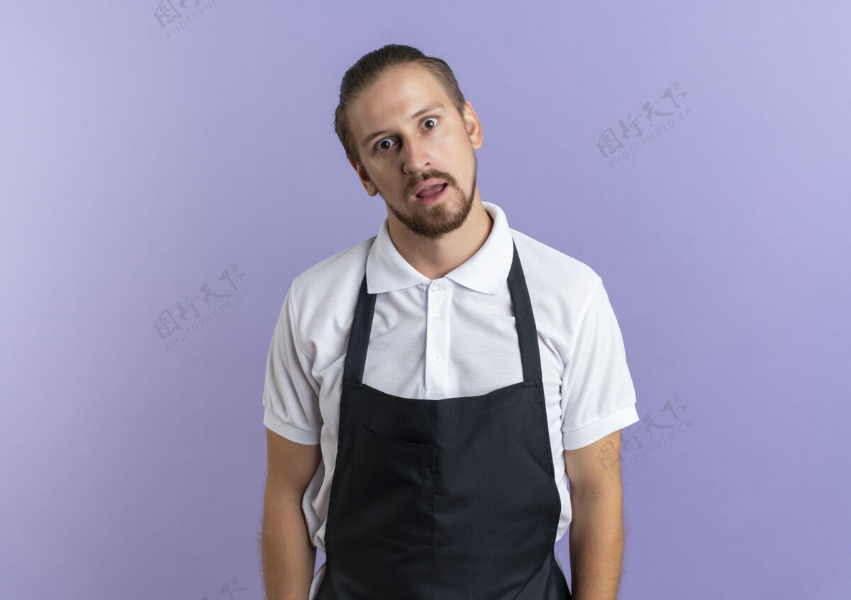 制服印象深刻的年轻英俊的理发师穿着制服站着 看着孤立的紫色与复制空间复制紫色理发师