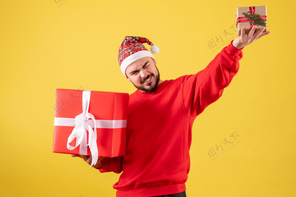 背景黄色背景下手持圣诞礼物的年轻男性正面图年轻男性欢乐人
