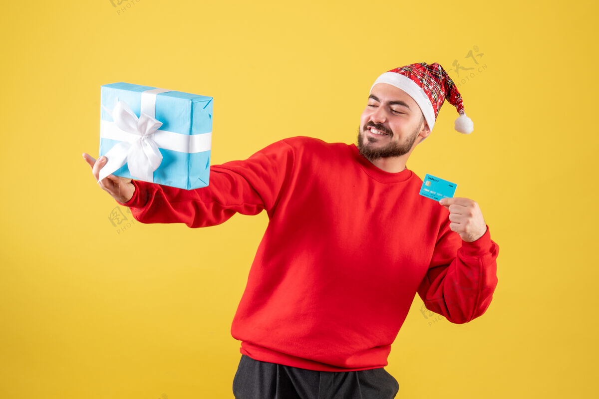 男性正面图年轻男子手持圣诞礼物和银行卡在黄色办公桌上礼物人人