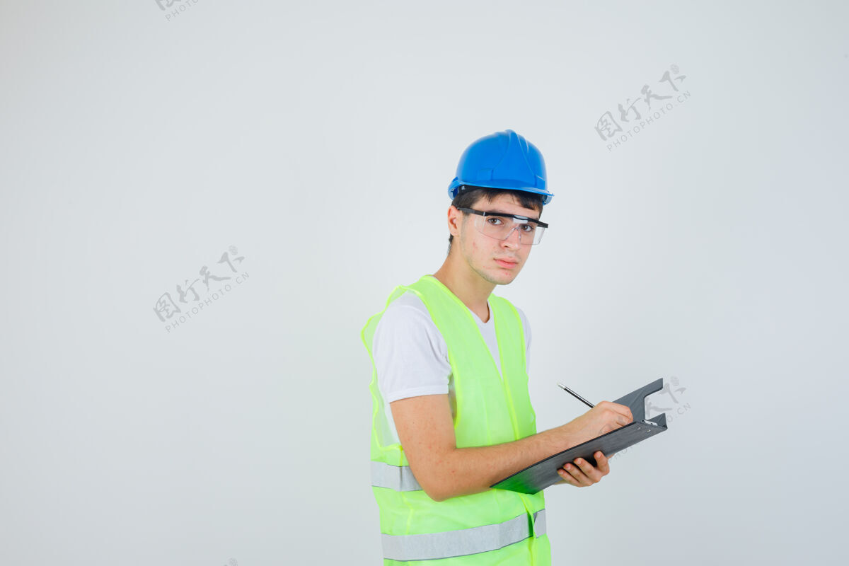 科技小男孩在文件夹里写笔记 看着穿着施工制服的相机 看着焦点前视图设备建筑男孩