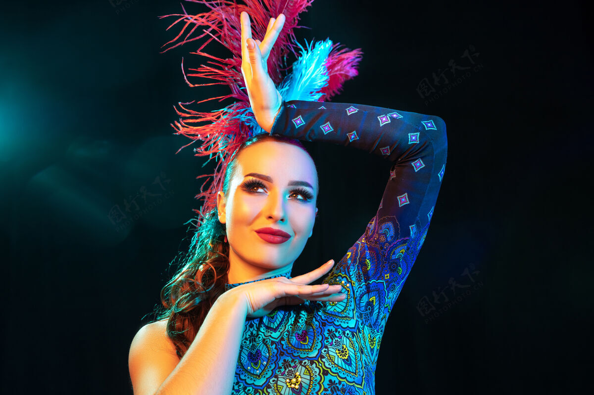 霓虹灯美丽的年轻女子在狂欢节和化装舞会服装在五颜六色的霓虹灯在黑墙上戏剧威尼斯人人类