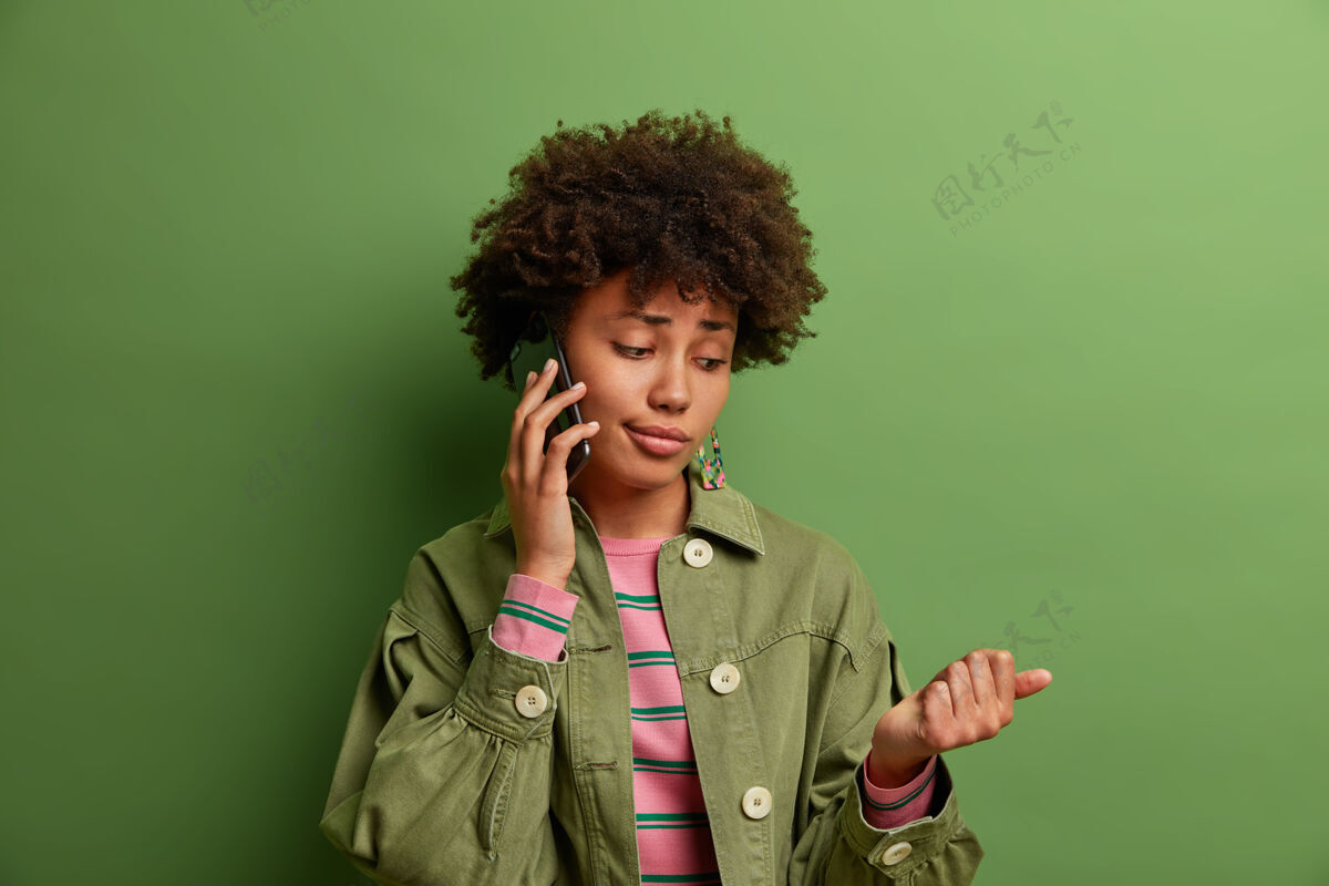 外卖无聊的非裔美国女人的室内镜头有电话交谈 看着她新修的指甲 不安的表情 穿着得体 站着杯子负片成人
