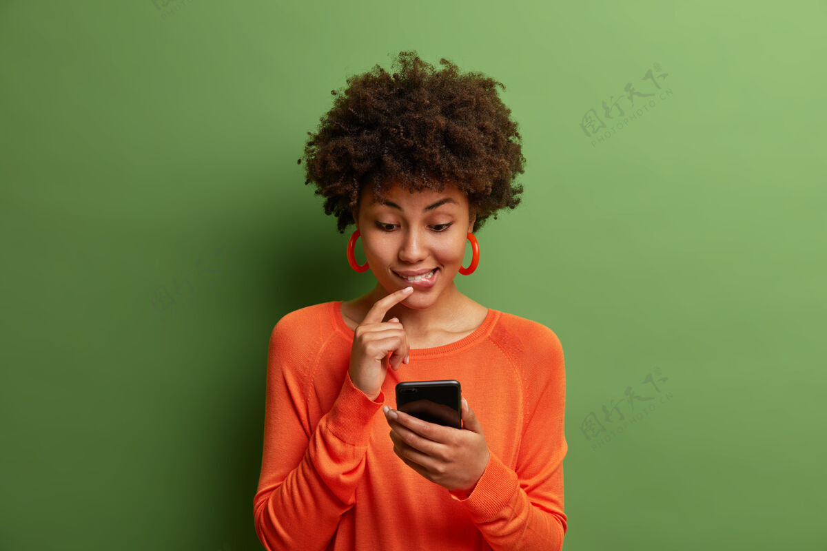评论通讯 科技 生活理念好奇的黑皮肤女人在网上看有趣的帖子 手里拿着手机 想着如何在收到的信息上给出答案 在室内摆姿势电话绿色民族