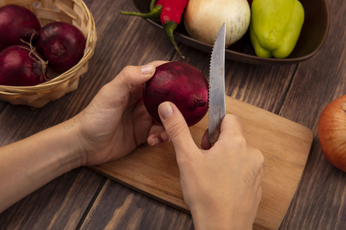 薯条俯视图中的女性手切割一个红色的洋葱在一个木制的厨房板上用刀在木墙上新鲜洋葱手