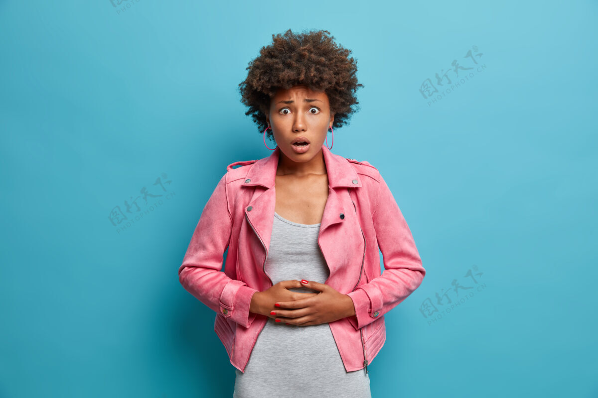 人吓坏了的卷发女人摸肚子 肚子疼得厉害 感觉不舒服 吃了变质的食物 看起来很困惑 有经期抽筋 胃美国月经
