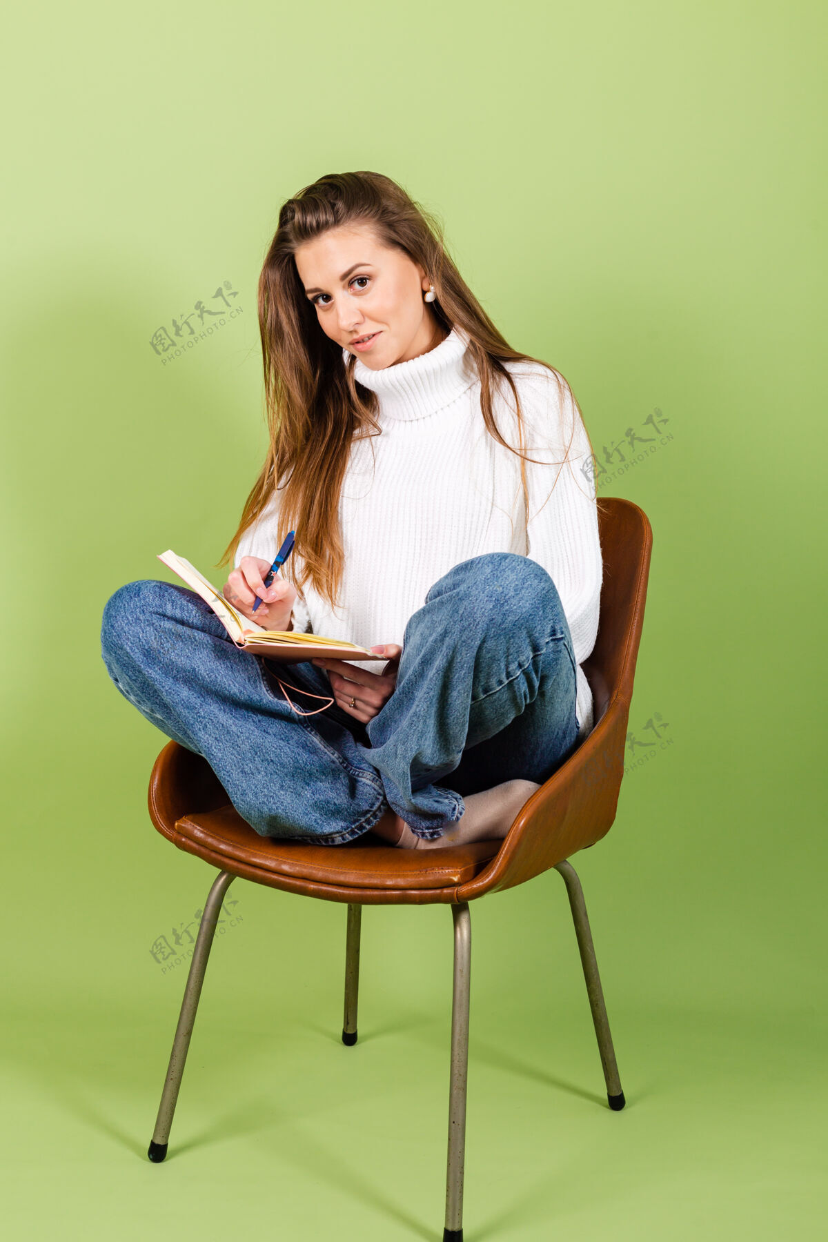 思想漂亮的欧洲女人穿着休闲的白色毛衣孤立 可爱快乐的坐在椅子上用记事本和笔学生教育狡猾