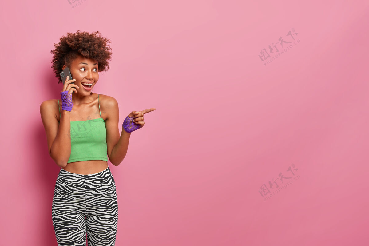 手套现代生活方式 科技和广告理念快乐的美国黑人妇女 卷发 穿着运动服 有电话交谈和旁听抱着姿势方式