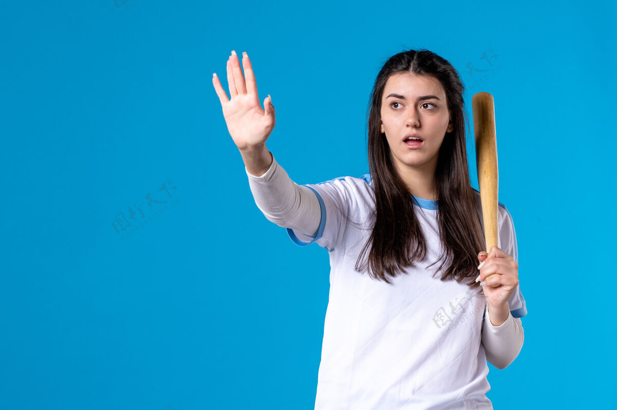 正面正面图蓝色墙上拿着棒球棒的年轻女子体育视图肖像