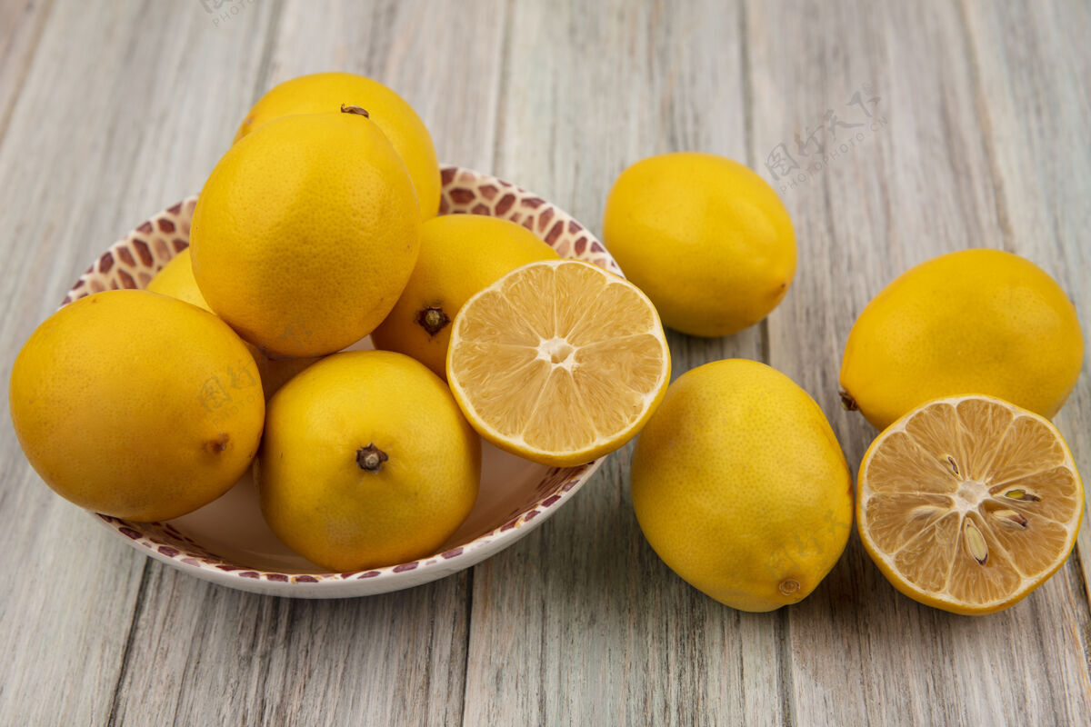 顶部半个和整个柠檬放在碗里的顶视图 柠檬被隔离在灰色的木墙上新鲜柠檬柑橘