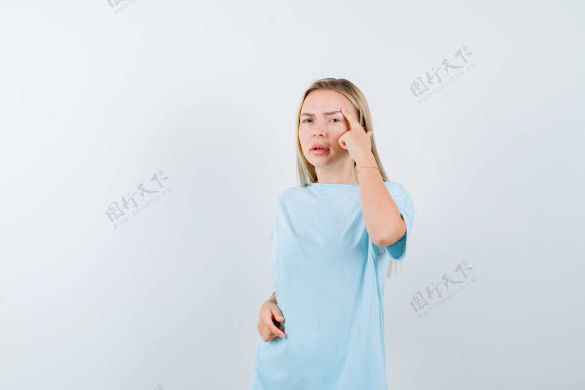 女孩穿着蓝色t恤的金发女孩把食指放在太阳穴上 面带沉思情感时尚女人