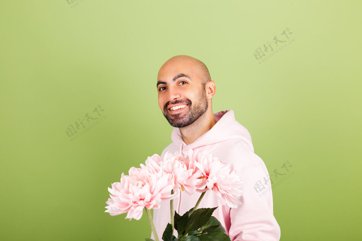 快乐年轻秃顶的白种人穿着粉色连帽衫孤身一人 捧着花束开心微笑花束男人享受