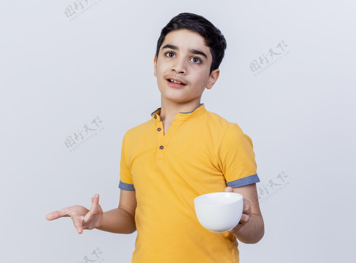 空间令人印象深刻的年轻高加索男孩拿着杯子看着和直指孤立的白色背景与复制空间复制指向年轻