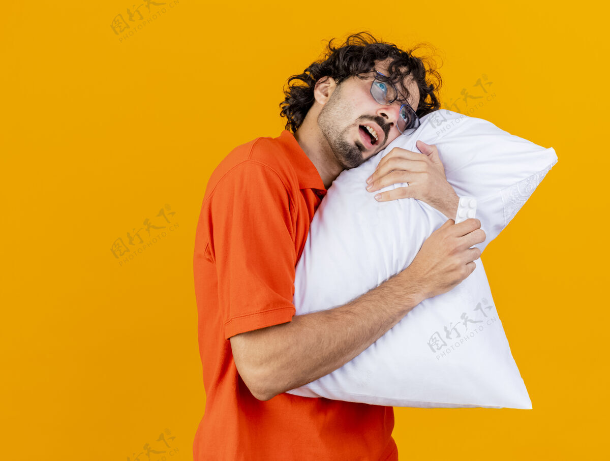 片虚弱的年轻白种人 戴着眼镜 抱着枕头和一包药片 头枕在枕头上 看起来笔直 橙色背景 有复印空间疾病枕头橙色
