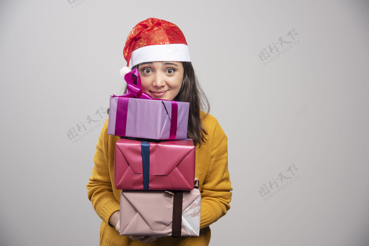 庆祝微笑的戴着圣诞帽的女人手里拿着礼品盒黑发快乐冬天