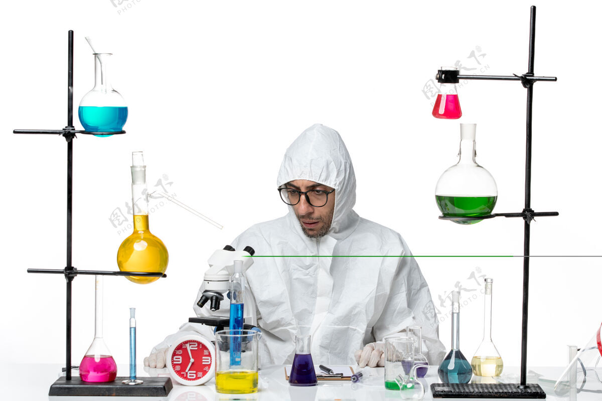 前面正面图穿着特殊防护服的男科学家围坐在桌子旁 拿着解决方案特殊化学烧杯