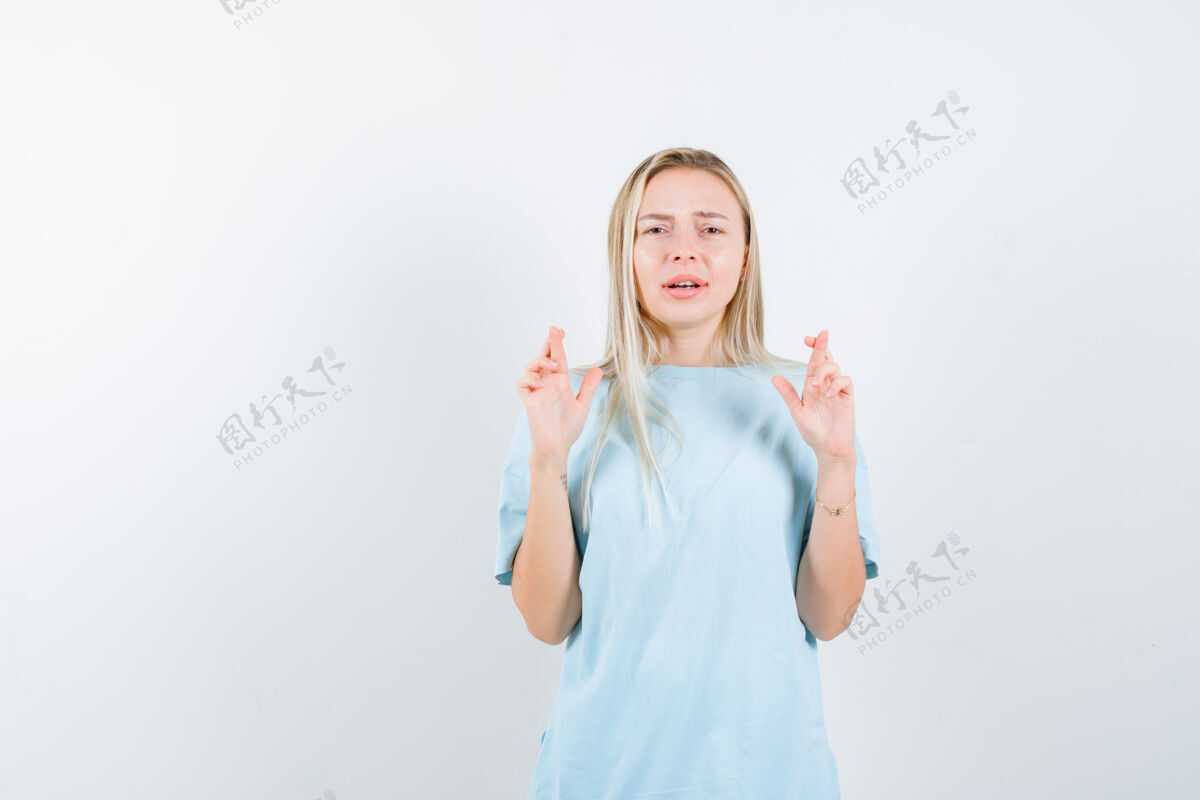 交叉年轻女士在t恤衫上交叉手指 看起来充满希望 正面视图手指微笑护理