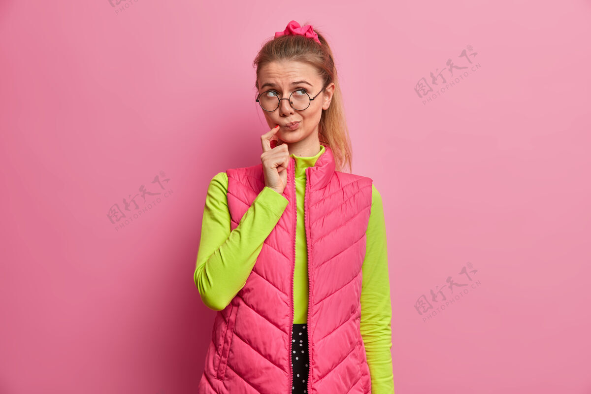 思考体贴的欧洲少女深思熟虑 面对困境 面带疑惑 戴着红眼镜 绿色套头衫 粉色背心 思考难题白种人怀疑女性