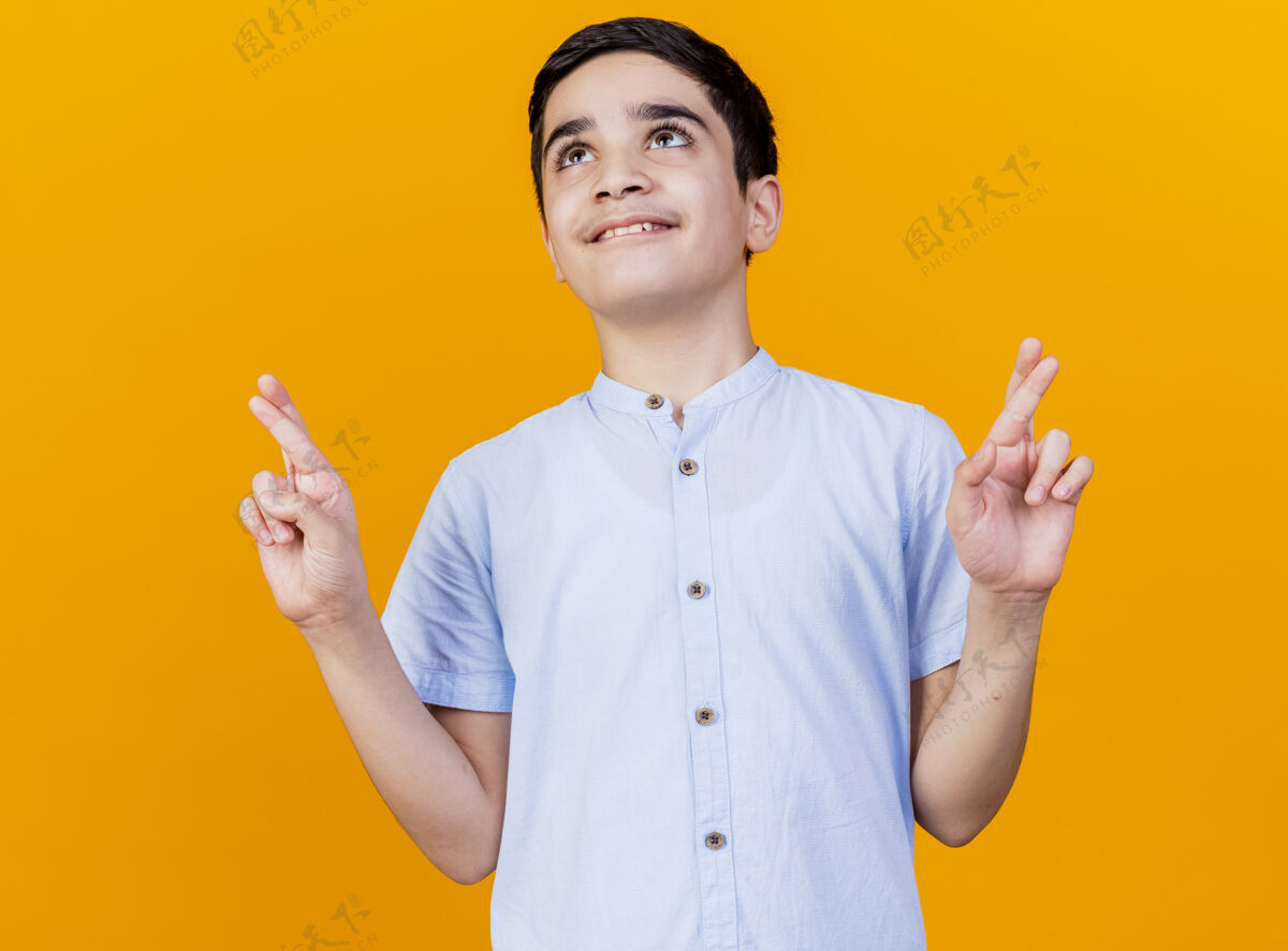 男孩微笑的年轻白人男孩仰望交叉的手指祈求好运孤立在橙色背景好年轻向上