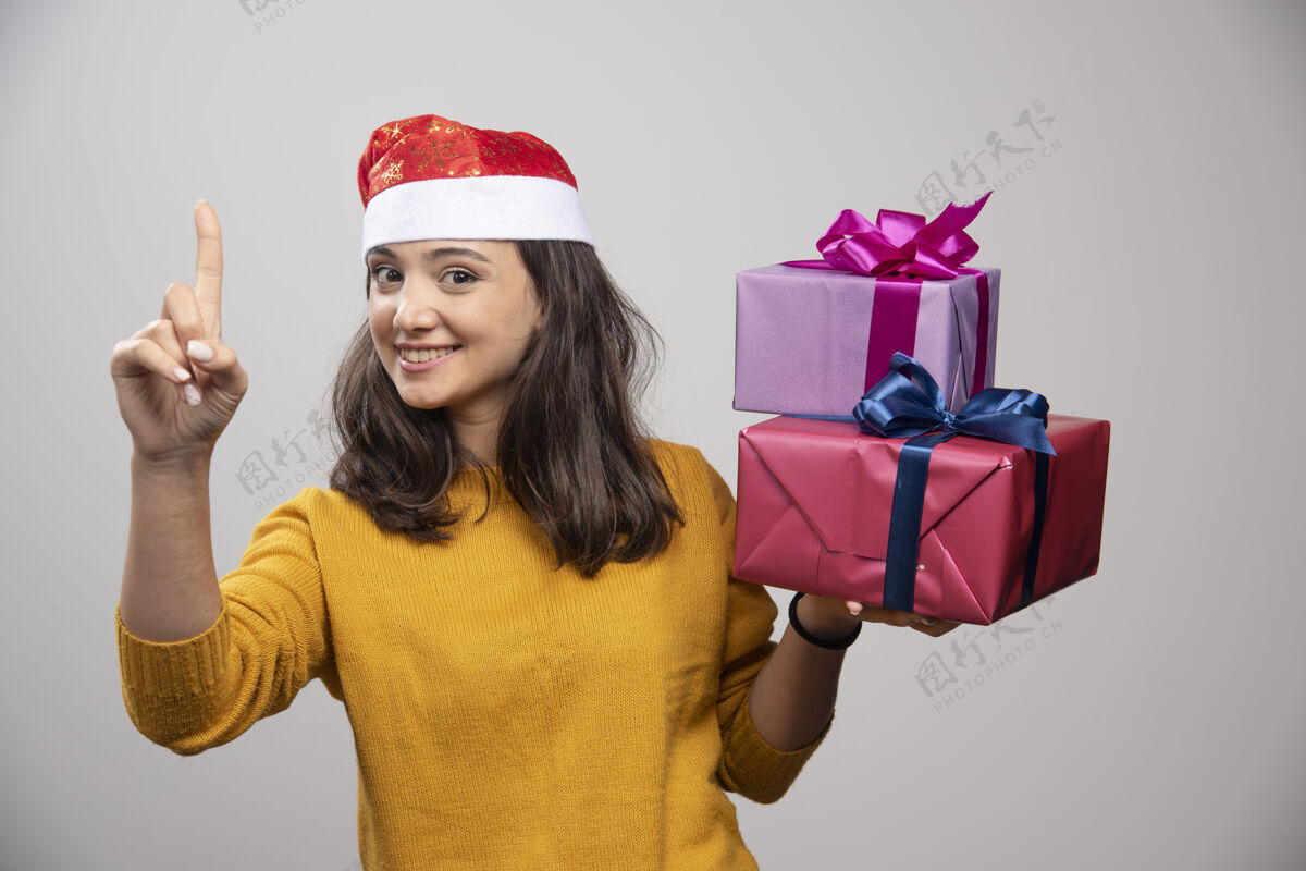 微笑带着圣诞礼物的戴圣诞帽的年轻女子模型黑发欢呼