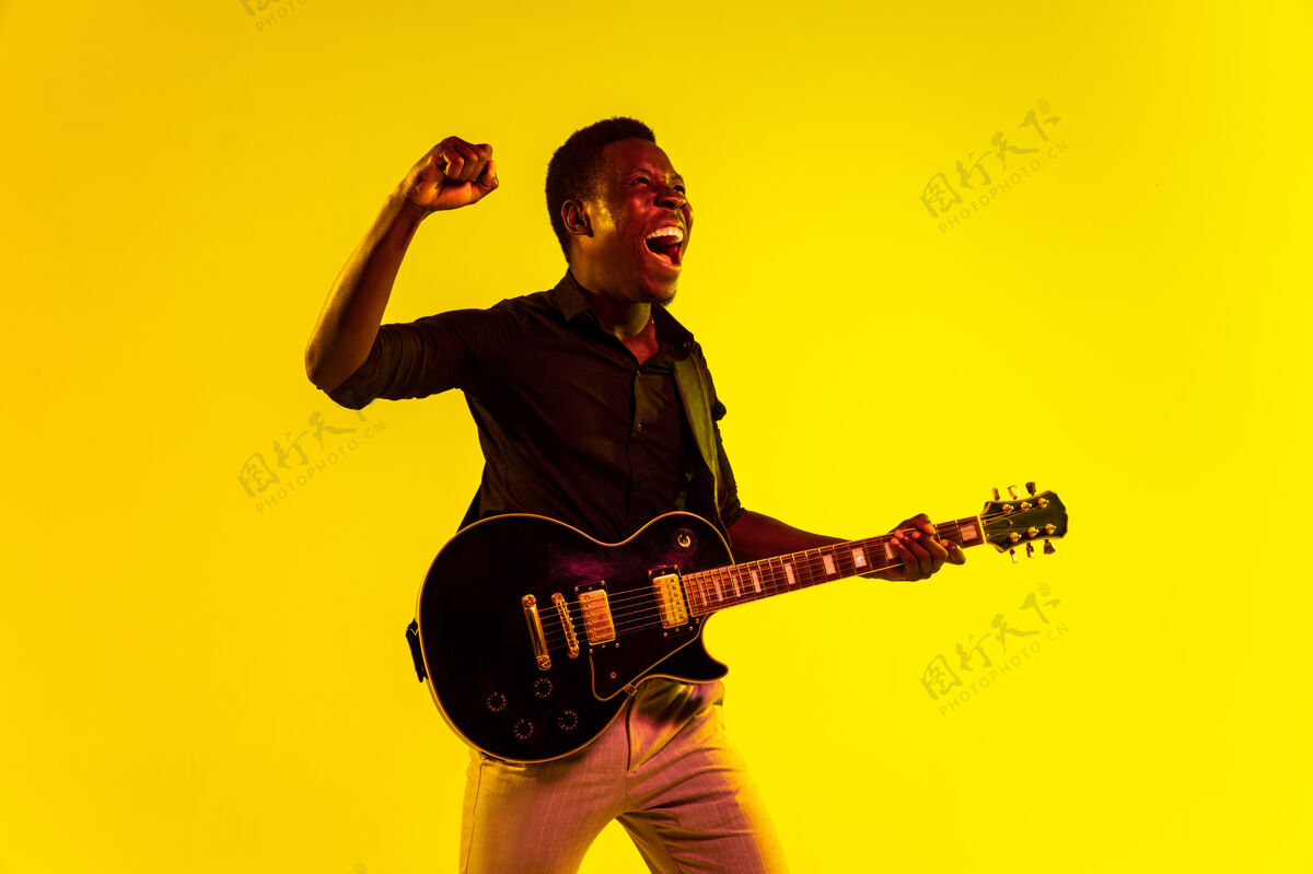 白天年轻的非洲裔美国音乐家在霓虹灯下像摇滚明星一样在黄色背景下弹吉他音乐家音乐黄色