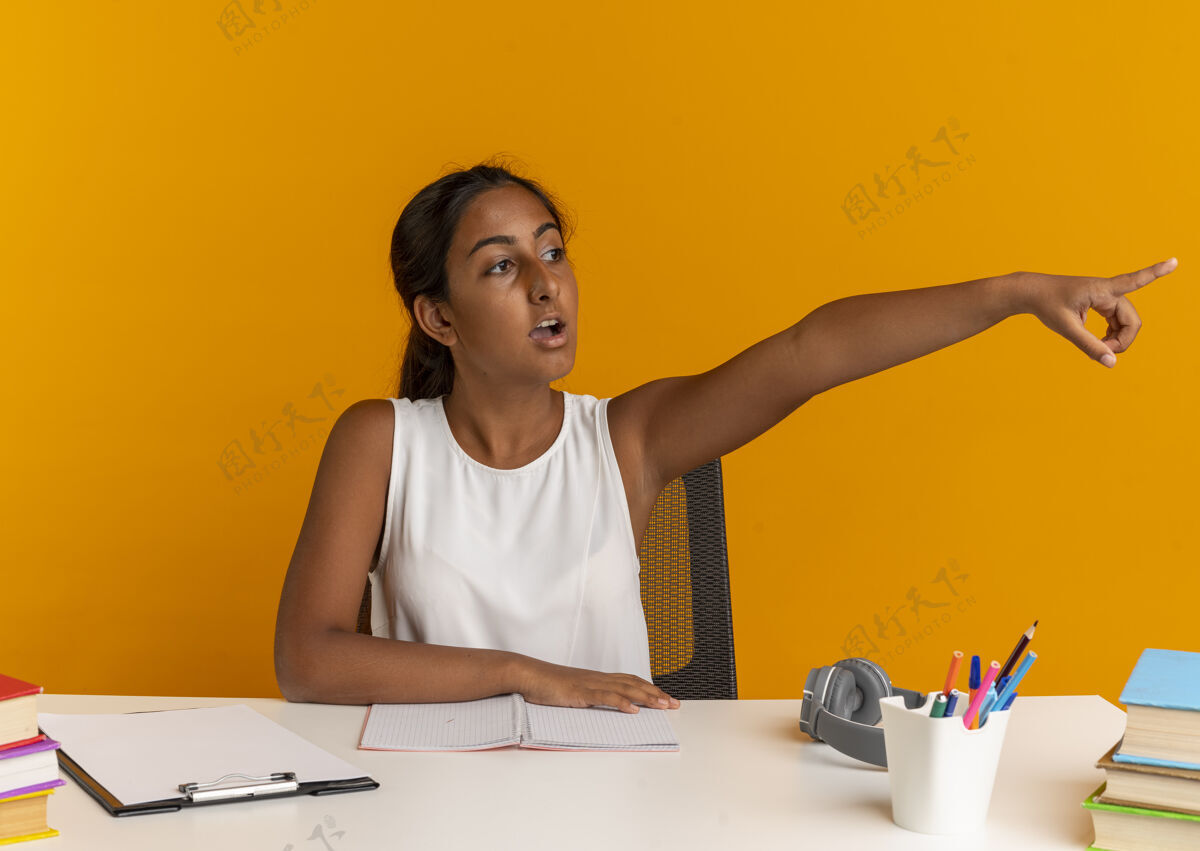 年轻想着坐在书桌旁的年轻女学生 手里拿着学习用具 指着旁边的桔子工具思考壁板