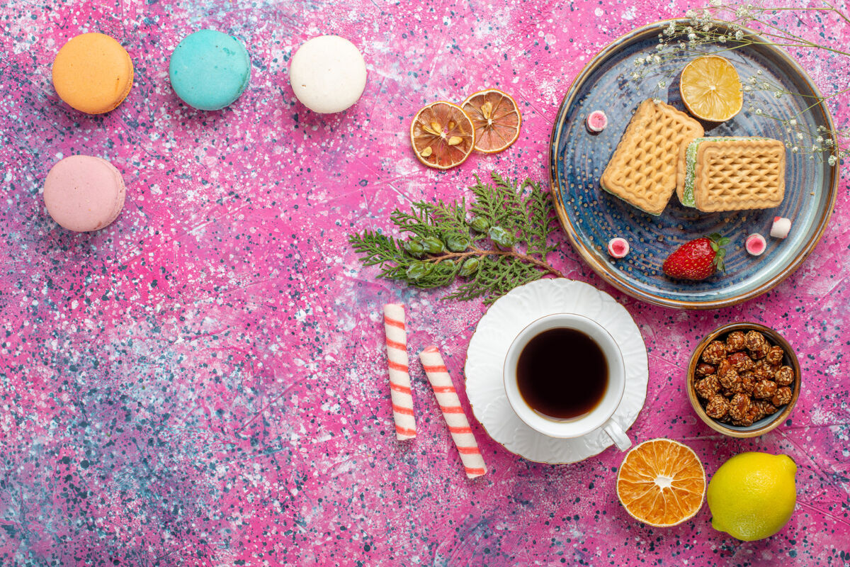食物粉色表面上有一杯茶和麦卡龙的甜华夫饼俯视图咖啡美味美味