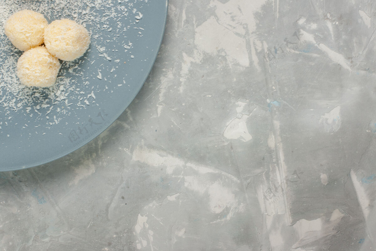 糖白色表面上蓝色盘子内美味椰子糖的俯视图冷的饼干水