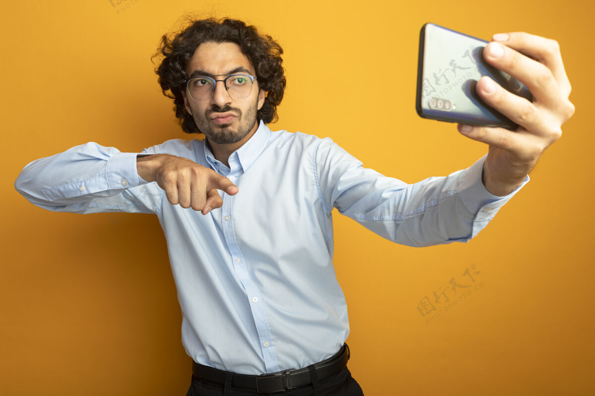 眼镜自信的年轻帅哥戴着眼镜自拍指着橙色墙上的电话自信指向采取