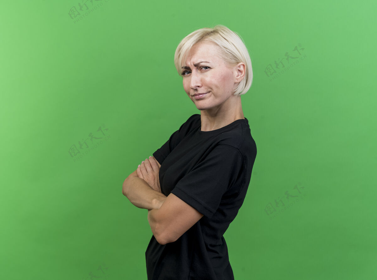 衣服眉头紧锁的中年金发女人站在侧视图中 紧闭的姿势看着隔离在绿色墙上的前面人女人表情