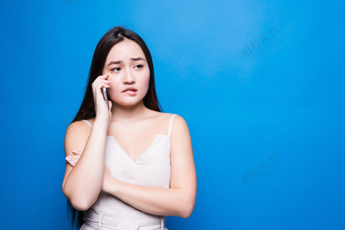 电话美丽的亚洲年轻女子在蓝墙上打电话电话悲伤不安
