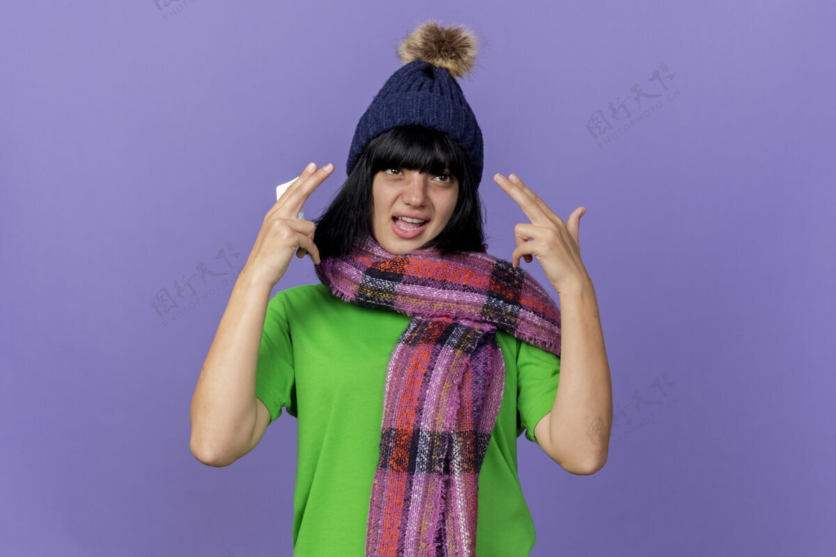 年轻人自信的生病的年轻女子戴着冬天的帽子和围巾看着身边拿着一包药片做着的手势孤立在紫色的墙上人疾病
