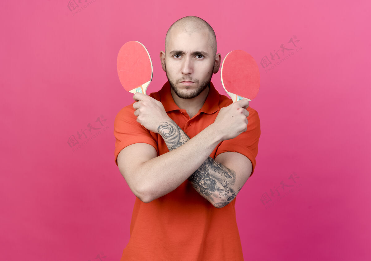 年轻自信的年轻人拿着乒乓球拍在粉红色的墙上横穿乒乓球墙运动