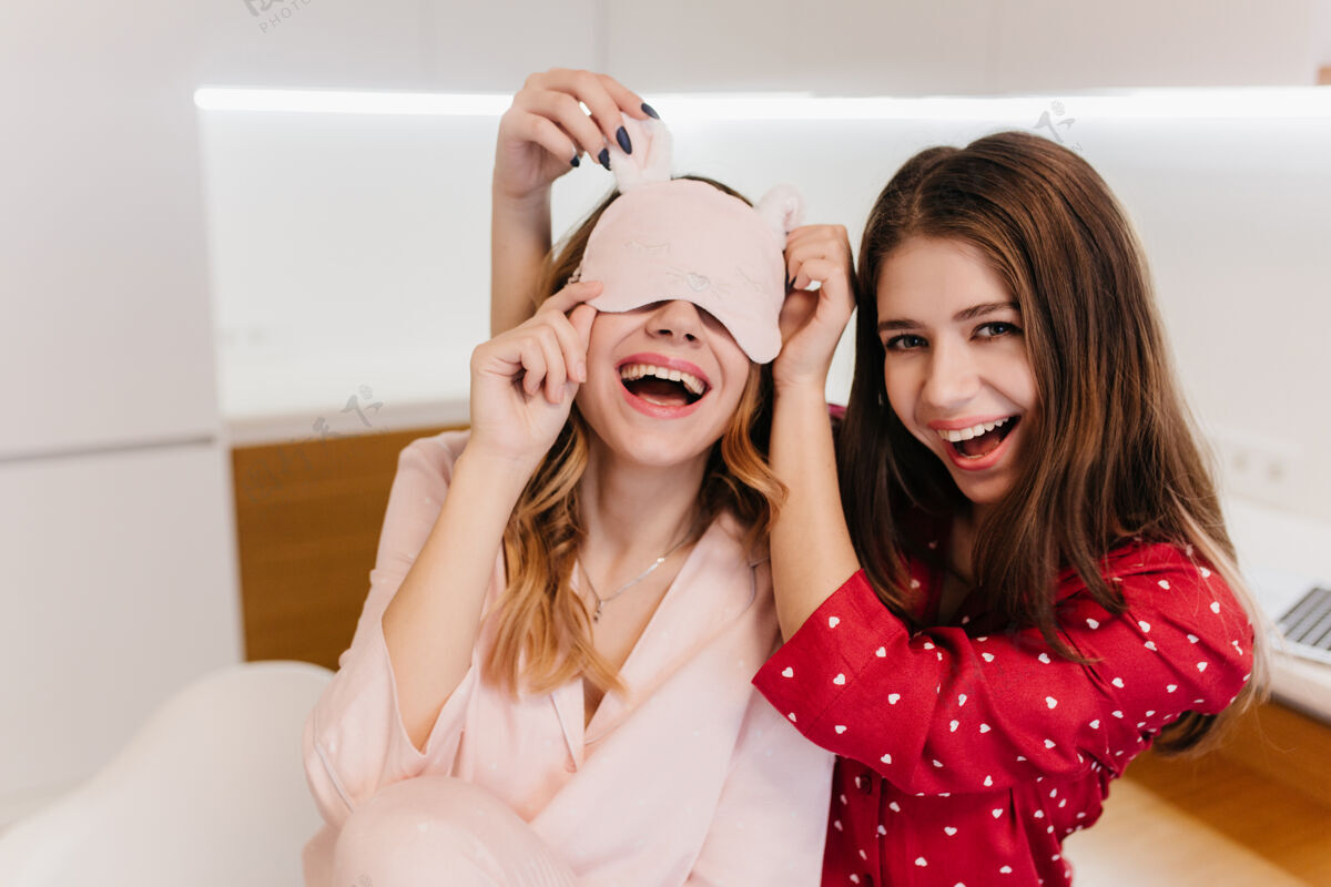 深色浪漫的棕色头发的女孩穿着红色睡衣 微笑着穿着睡衣嬉戏的姐妹们的照片享受舒适友谊