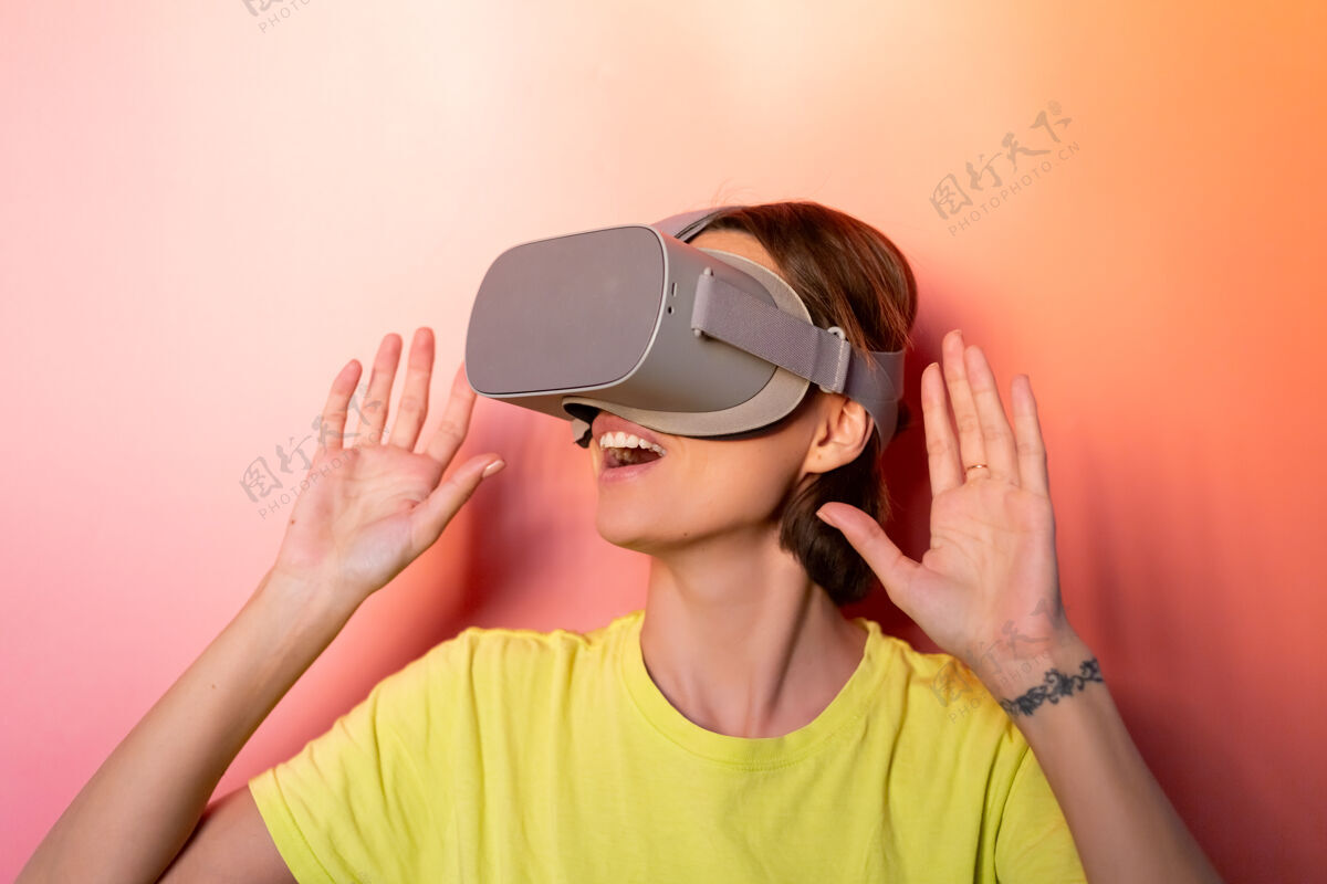 眼镜在粉红色橙色背景的工作室里 戴着虚拟现实眼镜的女人的情感肖像女性女孩护目镜