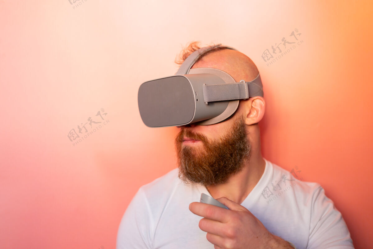 护目镜一个留着胡子的男人在工作室里戴着虚拟现实眼镜 背景是粉橙色的 这是一幅感人的肖像创新模拟成人