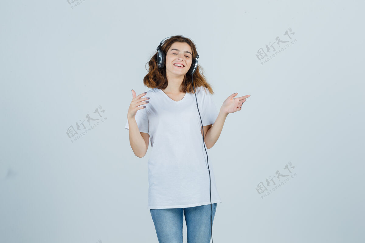 耳机年轻女性穿着白色t恤 牛仔裤 戴着耳机欣赏音乐 看起来很开心 正面照惊喜面部卷发