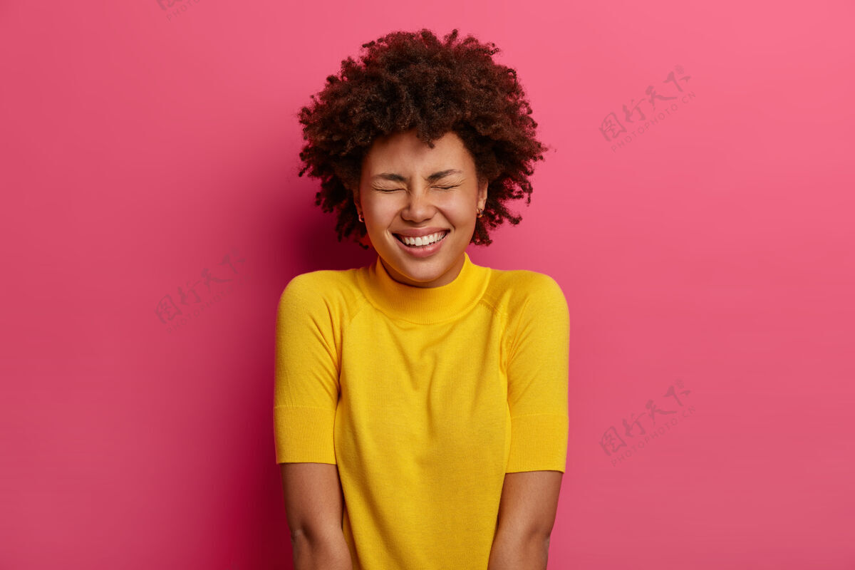 咯咯笑积极的非洲裔美国女人开心地笑着 笑着搞笑的笑话 穿着黄色的衣服 高兴地闭上眼睛 隔着粉红色的墙人 情绪和面部表情的概念温柔凝视种族