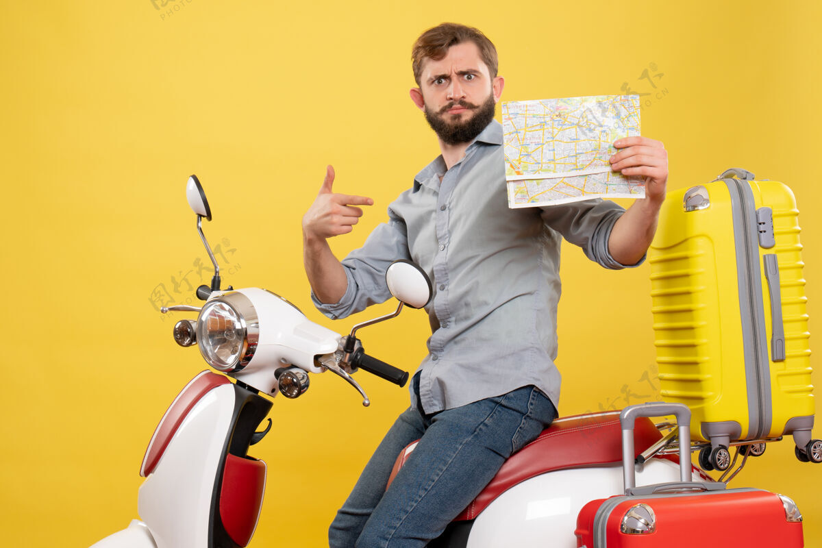 指向旅游概念与年轻的情感胡须男子坐在摩托车上 并指出它的黄色地图向前摩托车车辆旅游