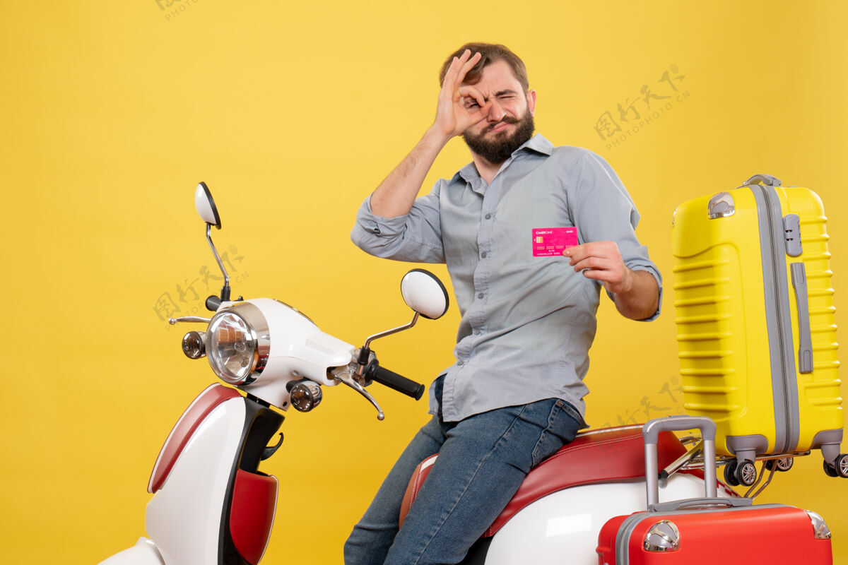 制造旅游概念与年轻的情感胡须男子坐在摩托车上 并持有银行卡在它的黄色手势年轻人车辆成人