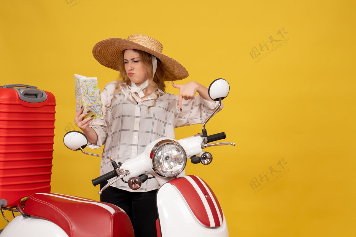 地图俯视图：雄心勃勃的年轻女子戴着帽子 坐在摩托车上 拿着地图做着“ok”的手势 收拾行李收集摩托车制造