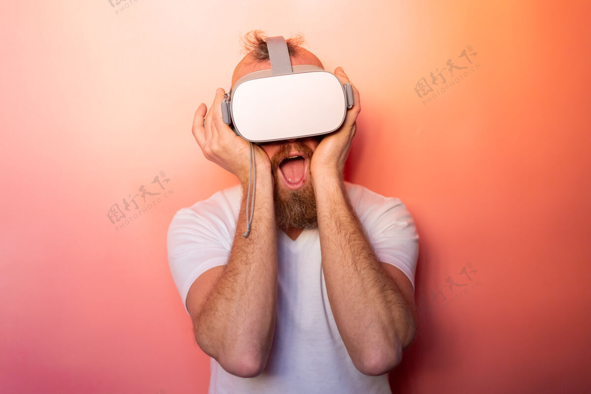 设备一个留着胡子的男人在工作室里戴着虚拟现实眼镜 背景是粉橙色的 这是一幅感人的肖像可穿戴合成活动
