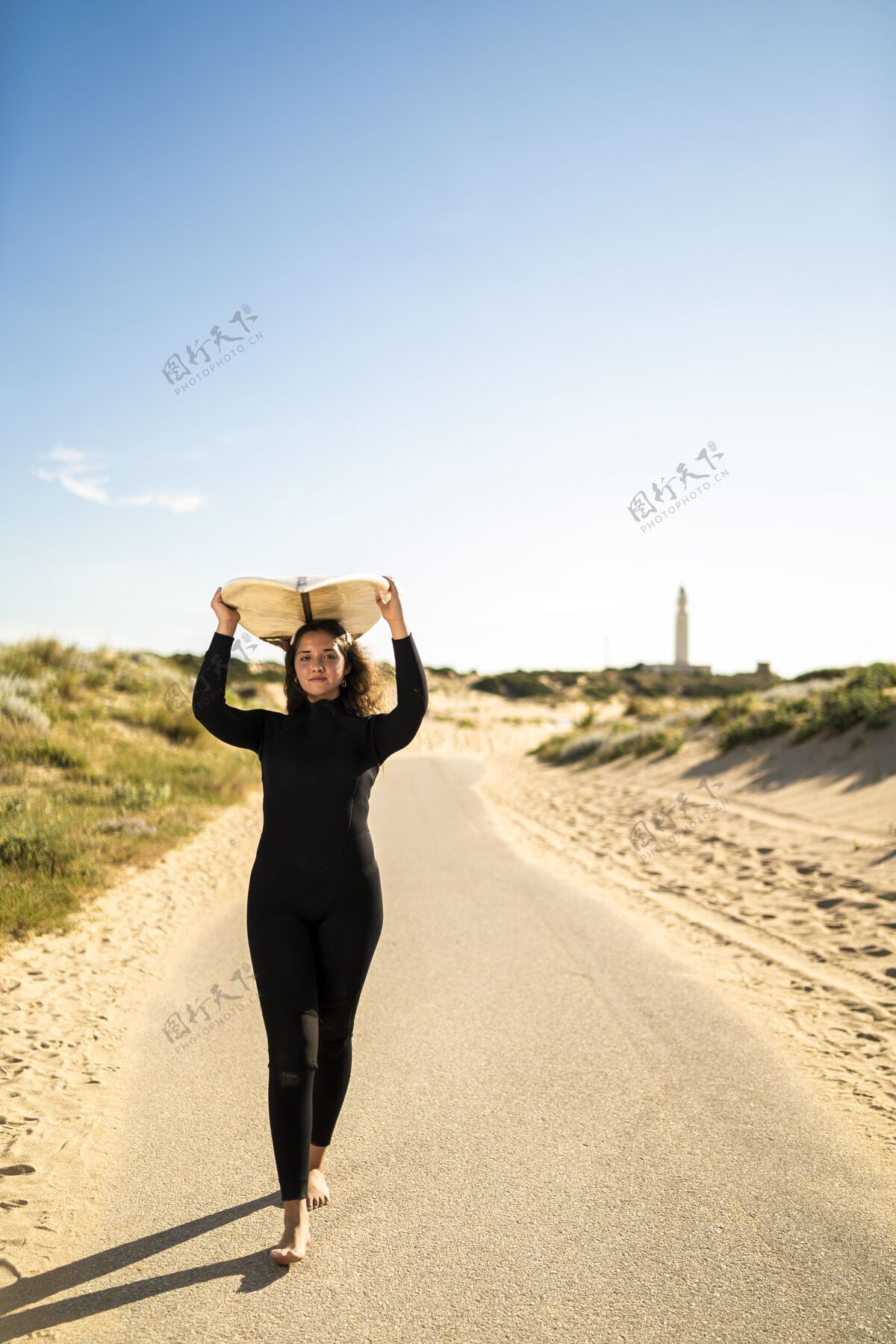 沙滩一个迷人的女性头上举着冲浪板的垂直镜头模特冲浪者散步
