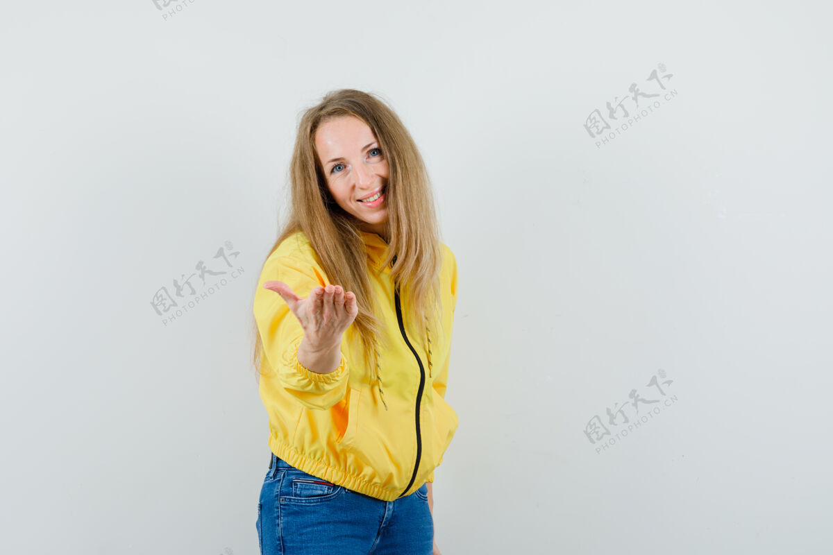 手身着黄色棒球服和蓝色牛仔裤的年轻女子向镜头伸出手 看上去很开心正面图年轻模特女性