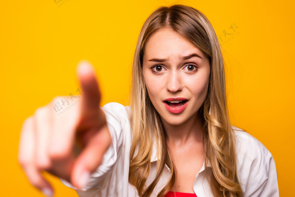 手指一个穿着t恤衫 张嘴指着黄色墙壁的快乐女人抱着20多岁可爱